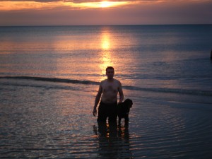 Brad kneeling in the water with Trixie by his side, sun setting in the background