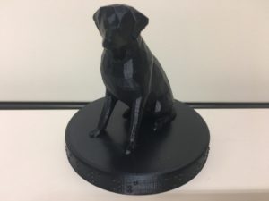 Statue of a black lab sitting on a little round base with "Trixie-Always in our hearts" written in Braille around the outside.